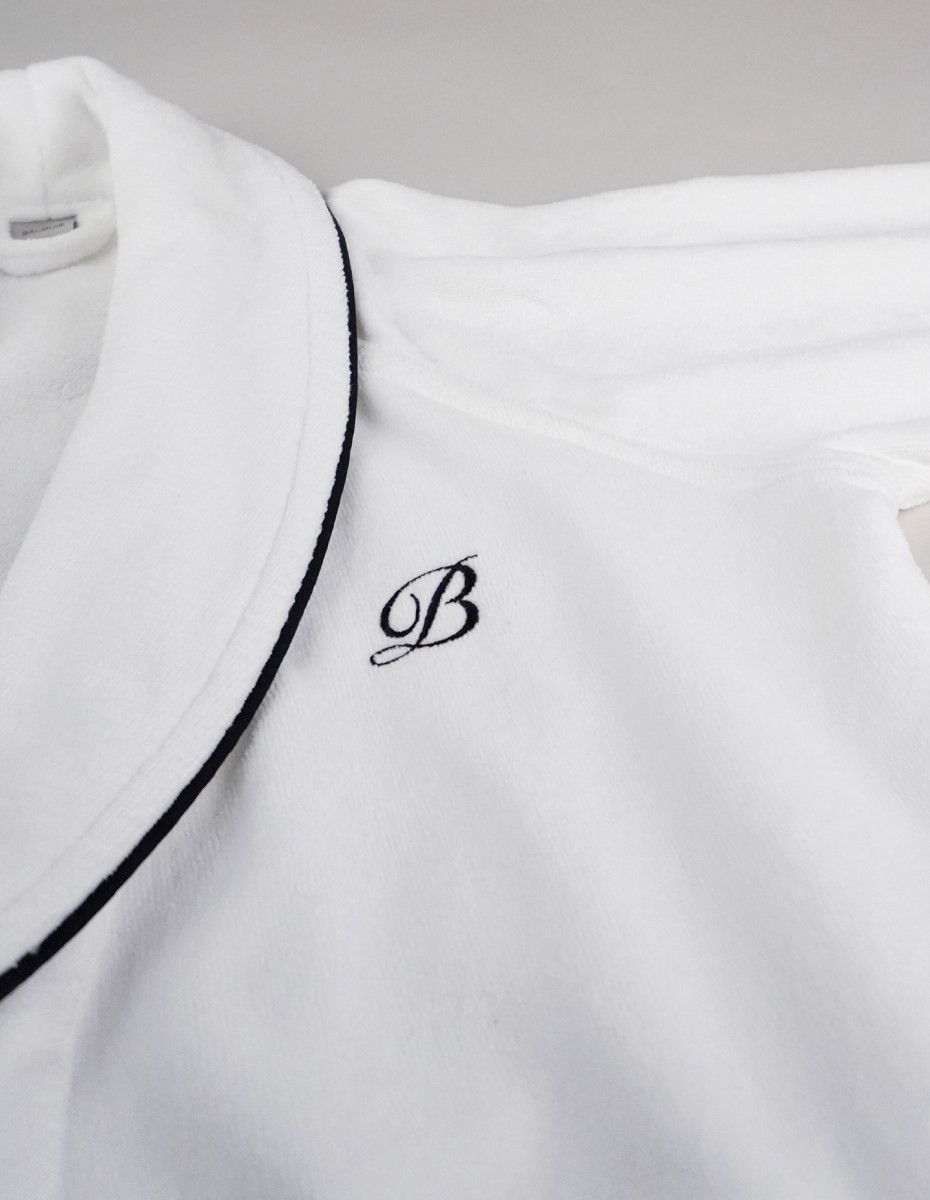 balmuir_portofino_robe_white_closeup_2_web Der Bademantel Portofino besteht aus 100 % Baumwolle. Das Bademantel-Design zeichnet sich durch einen markanten Schalkragen und einen passenden Gürtel aus. Es ist mit Paspeldetails am Schalkragen und an den Ärmeln sowie einem raffiniert gestickten Markenlogo versehen. Unsere Portofino-Bademäntel werden in Portugal in perfekter Handarbeit gefertigt.